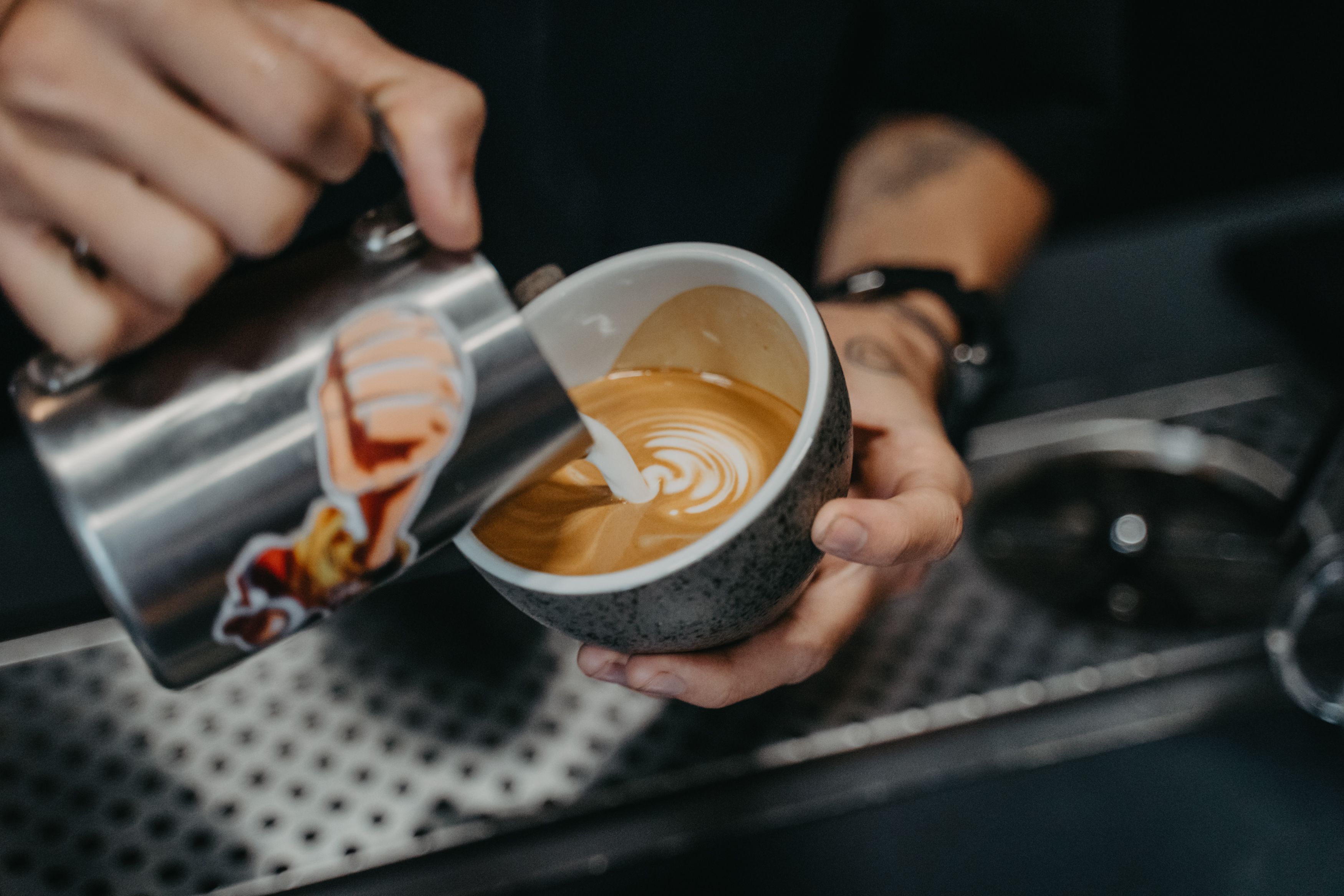 Barista carefully pouring latte art into a ceramic cup, showing hand-crafted personalized coffee