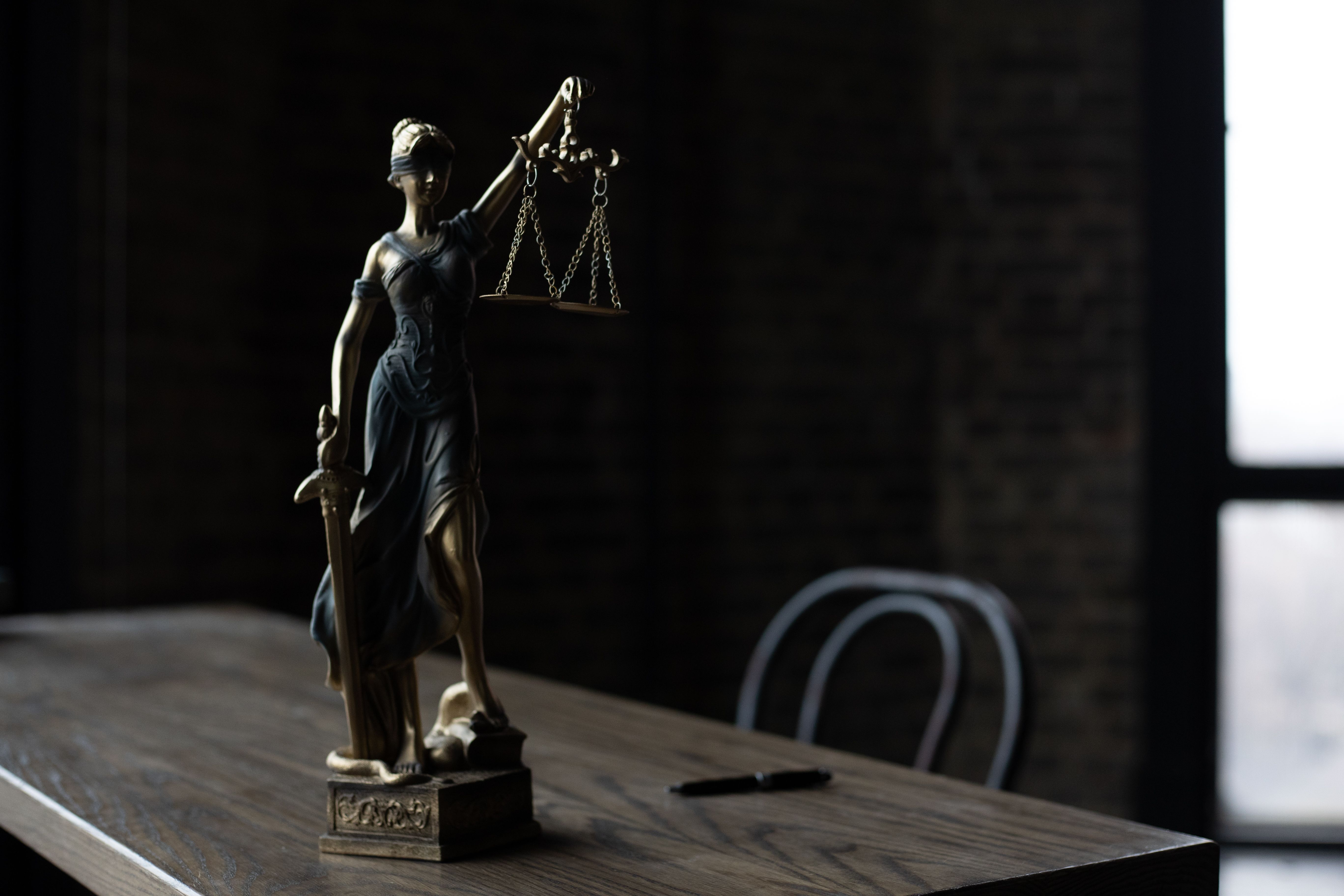 Lady Justice figurine on a wooden table in a dimly lit room, symbolizing fairness and ethics in legal funding