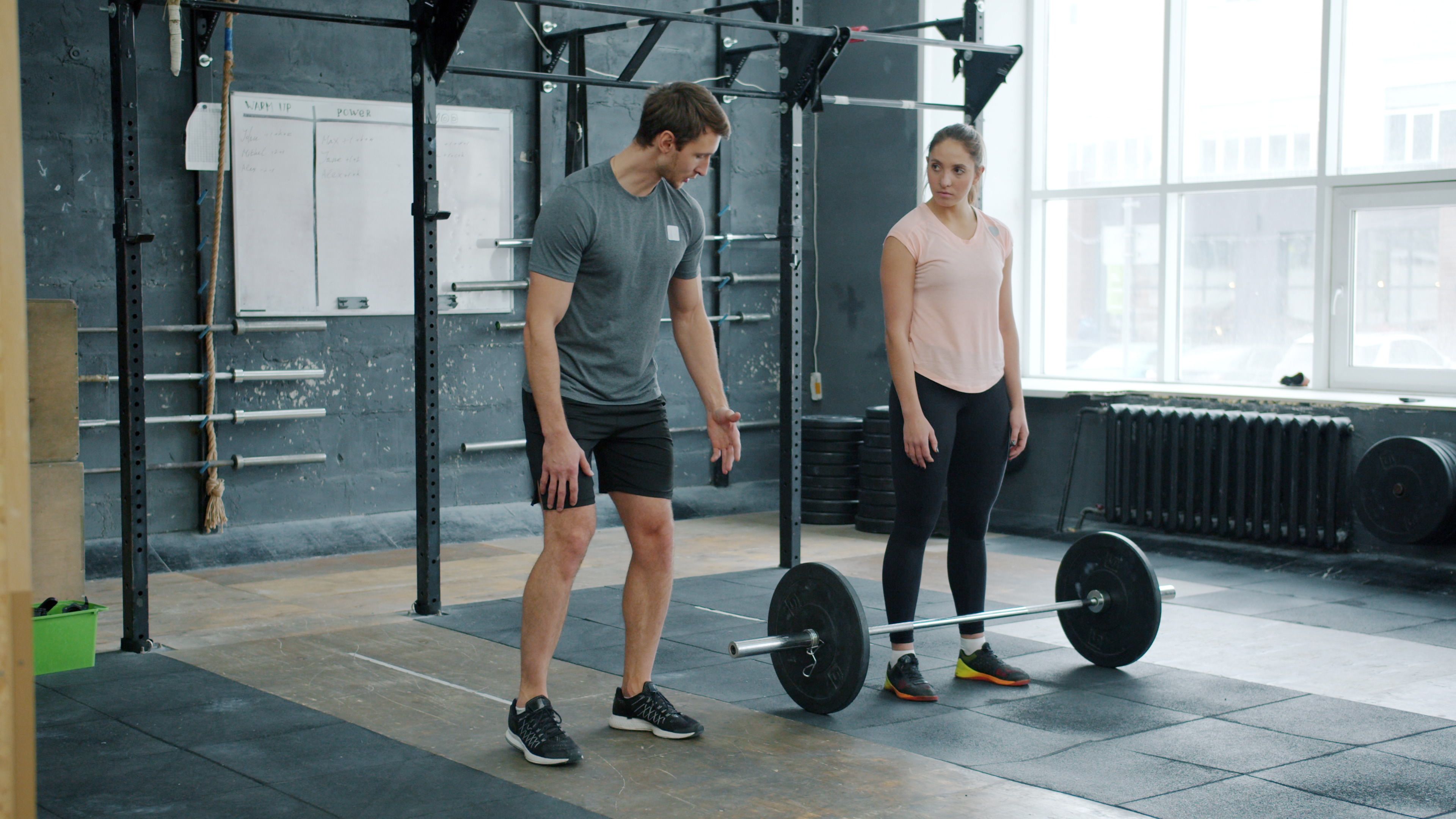 A personal trainer instructing a client on barbell lifting technique in a gym