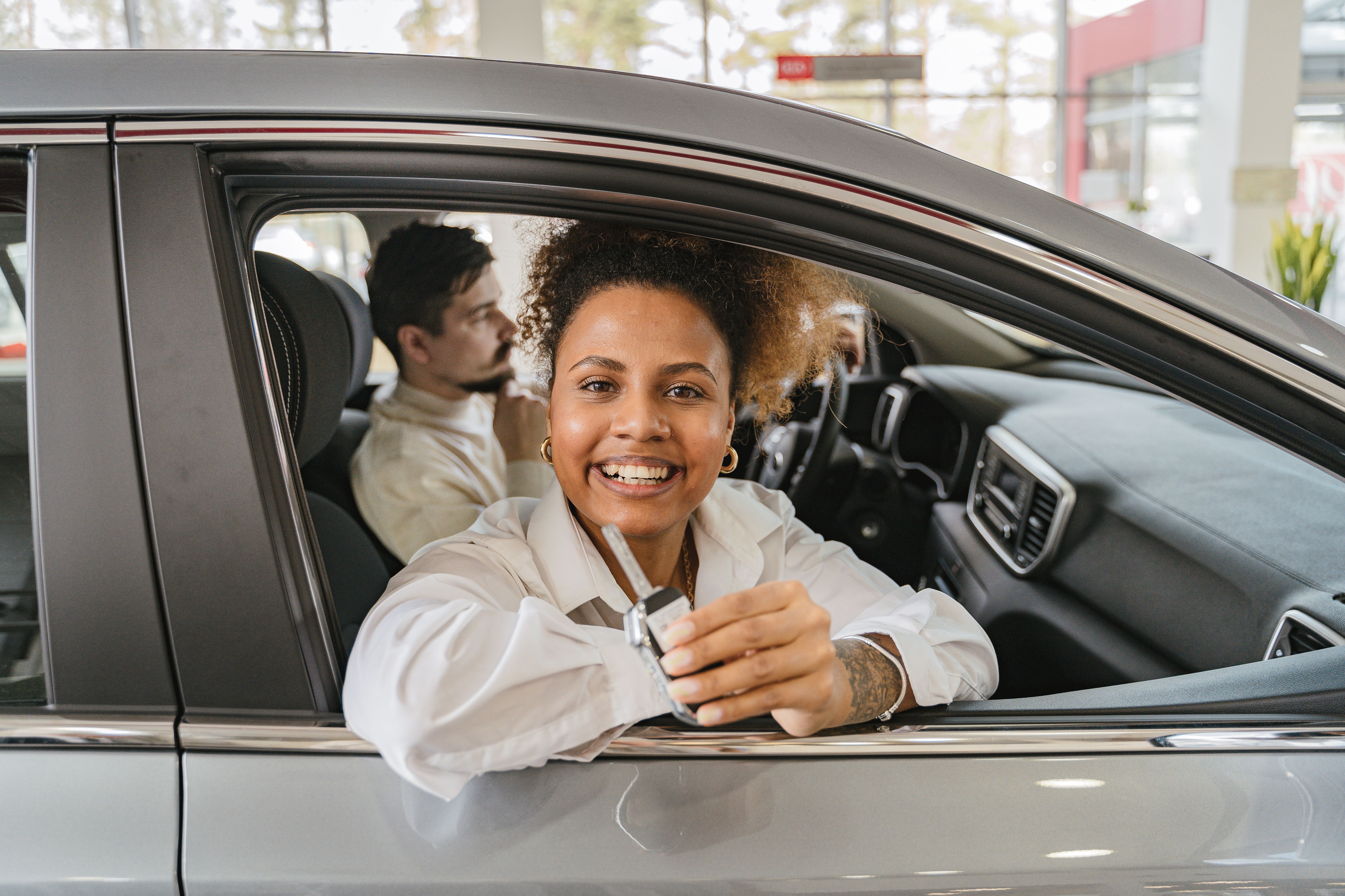 Joyful couple holding car keys in their new car in a dealership showroom