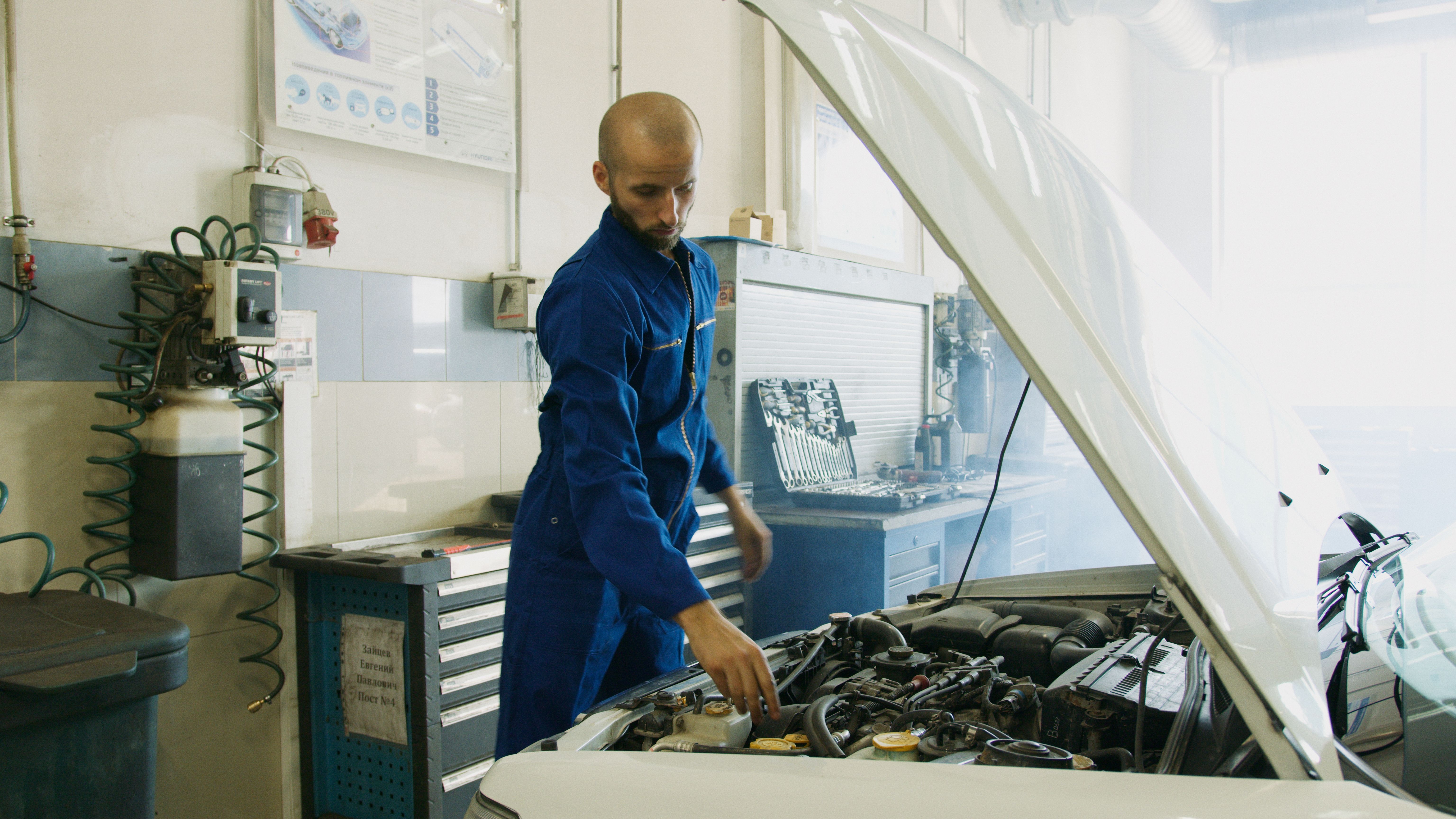Mechanic in blue uniform inspecting a car engine in a workshop
